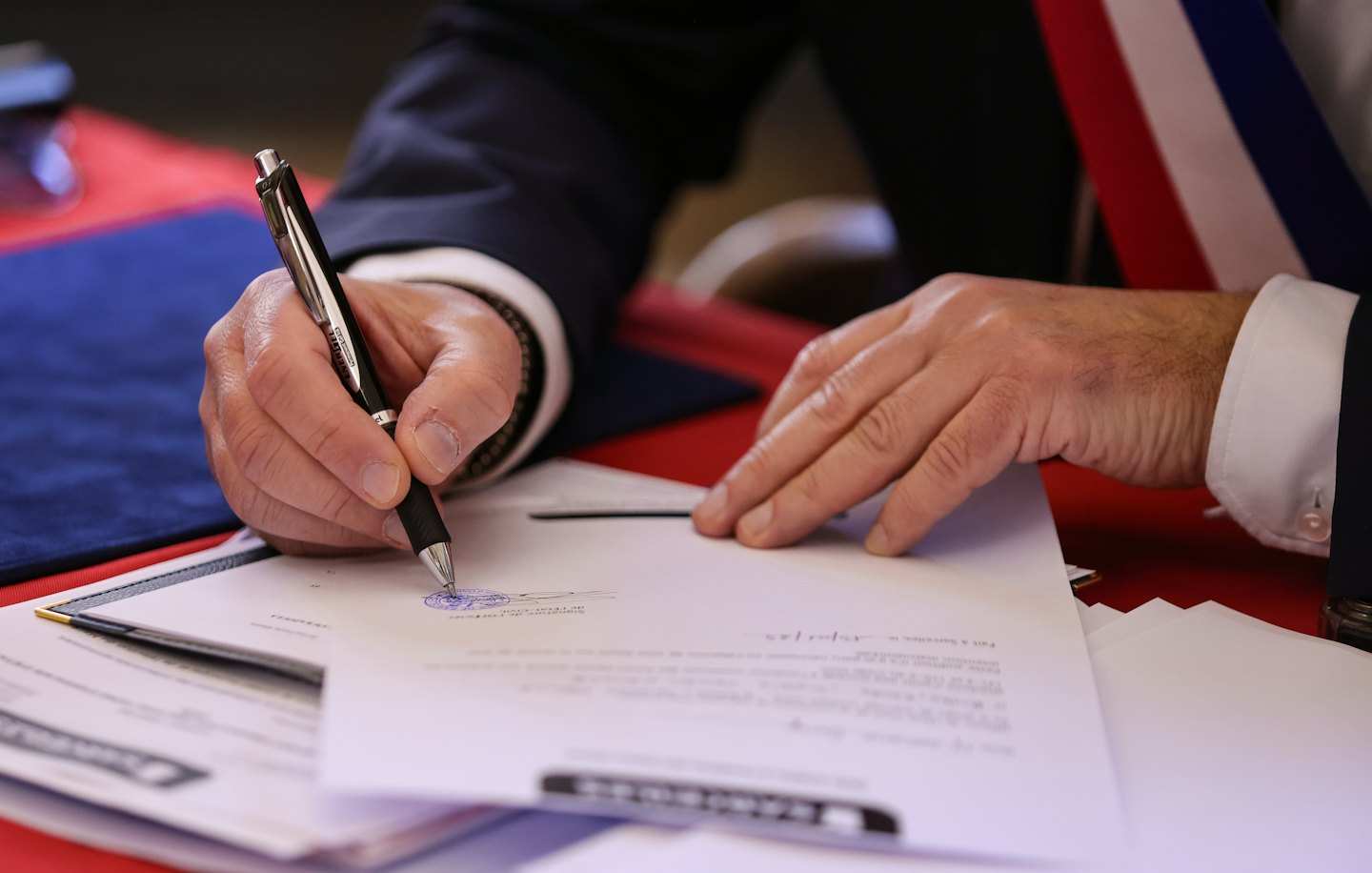 Un professionnel signe un document officiel à une table rouge.
